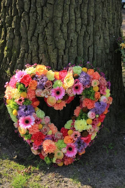 Heartshaped pastel sympathy flowers  or funeral flowers near a tree