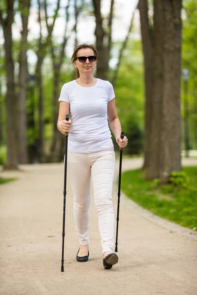 活跃妇女在白色休闲穿戴散步在公园用旅游棍子 — 图库照片