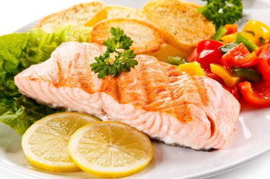 Grilled salmon with croutons, fresh vegetables and lemon slices on white plate clipart