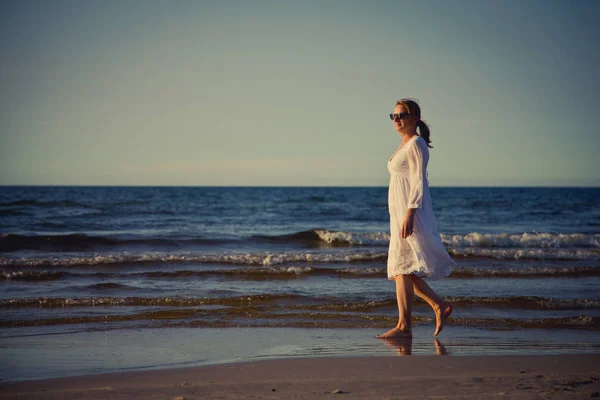 穿着白色连衣裙的女人在海边散步 — 图库照片