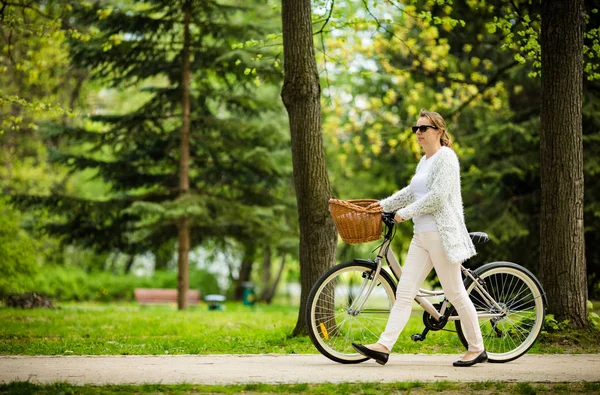 自転車で公園を歩いて着用する白いカジュアルでアクティブな女性の側面図 — ストック写真