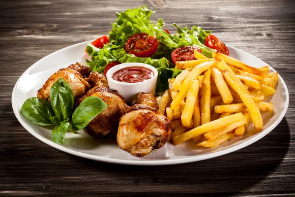 Roasted chicken legs with french fries, barbecue sauce and fresh vegetables on white plate on wooden table