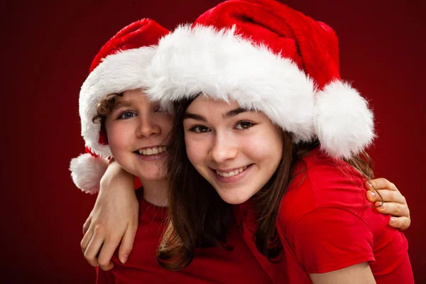 Deux Enfants Dans Santa Chapeaux Câlins Sur Dégradé Fond Rouge — Photo