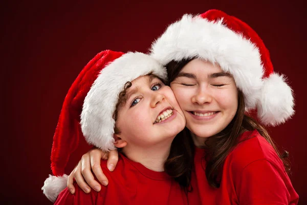 Duas Crianças Chapéus Papai Noel Abraçando Gradiente Vermelho Preto Fundo — Fotografia de Stock