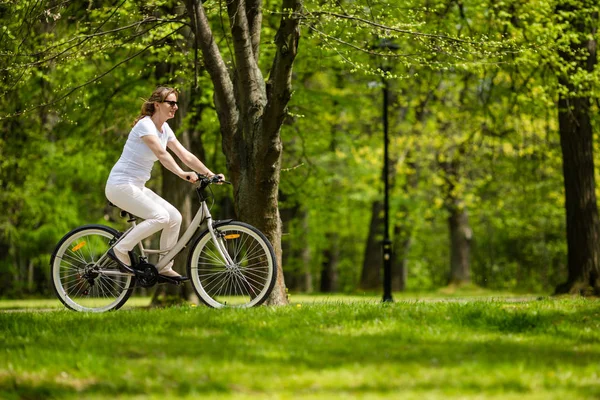 春の公園で女性の自転車に乗ってカジュアルな服装で大人の女性 — ストック写真