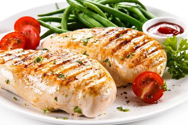 Grilled chicken fillet with tomatoes, green peas and ketcuh on white plate