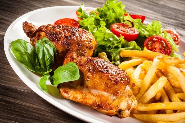 Fried chicken thighs with french fries and fresh salad on white plate