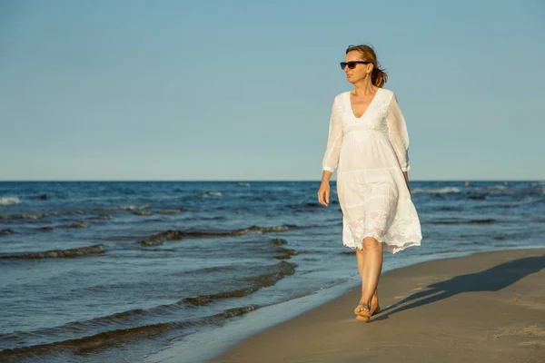 海辺で歩いている白いドレスの大人の女性 — ストック写真