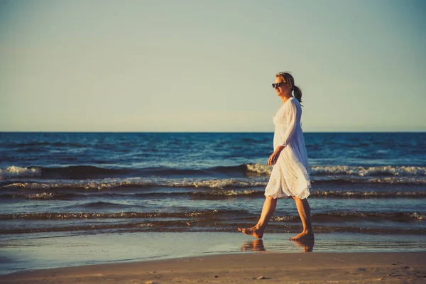 穿着白色礼服走在海边的成年妇女 — 图库照片