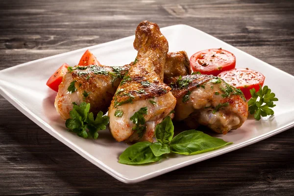 Grilled chicken legs with cherry tomatoes and herbs on white plate on wooden table