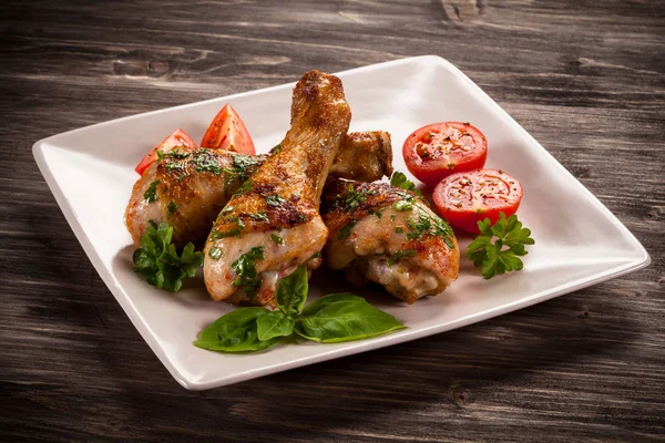 Grilled chicken legs with cherry tomatoes and herbs on white plate on wooden table