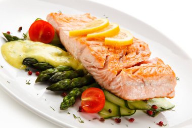 Baked salmon with asparagus, fresh tomatoes, lemon slices on white plate clipart