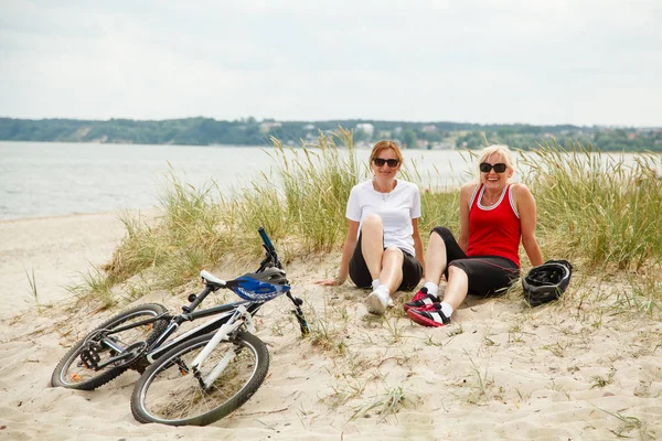 Duas Mulheres Meia Idade Óculos Sol Descansando Praia Perto Bicicleta — Fotografia de Stock