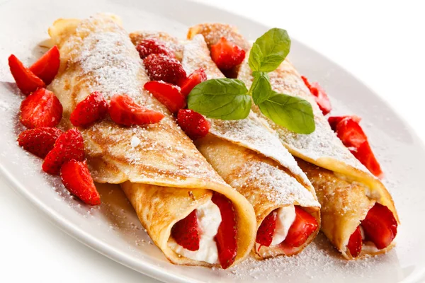 Sweet crepes stuffed with strawberries and cream on white plate