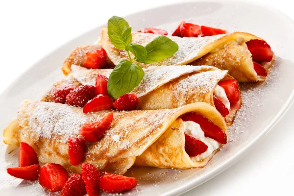 Sweet crepes stuffed with strawberries and cream on white plate