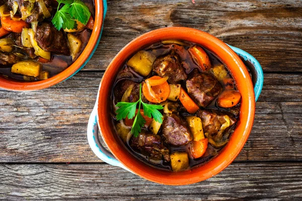 Roast pork cheeks with carrots and celeriac in sauce on wooden table