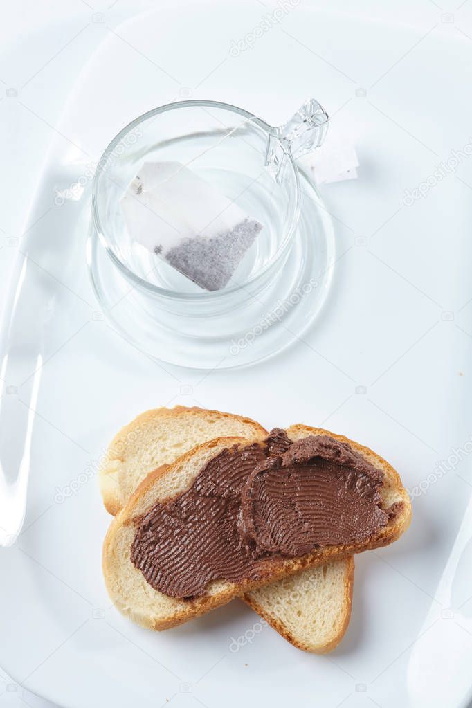 glass with teabag and bread with chocolate on plate, breakfast concept