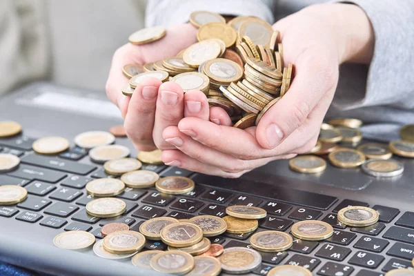 Hands holding pile of coins over laptop