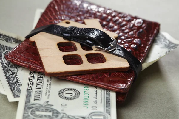 wallet with money and wooden house toy wrapped with belt, close-up
