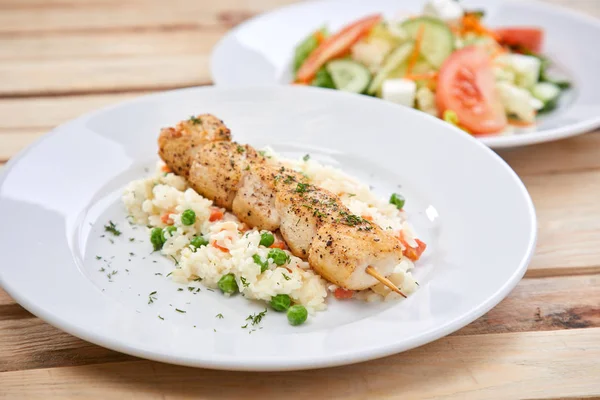 chicken kebab with rice and salad on white plates, close-up