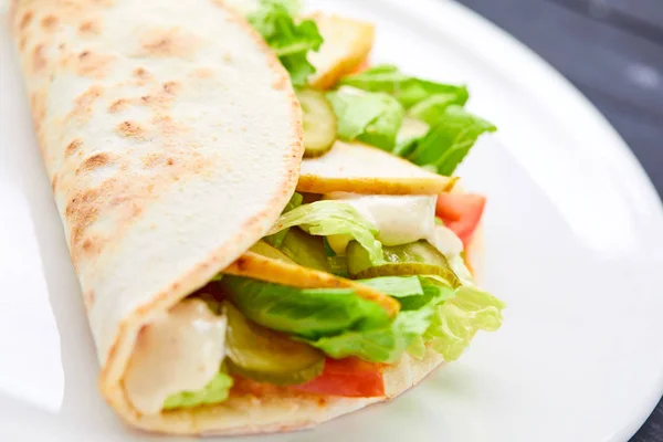 sandwich wrap with meat and vegetables on white plate, close-up