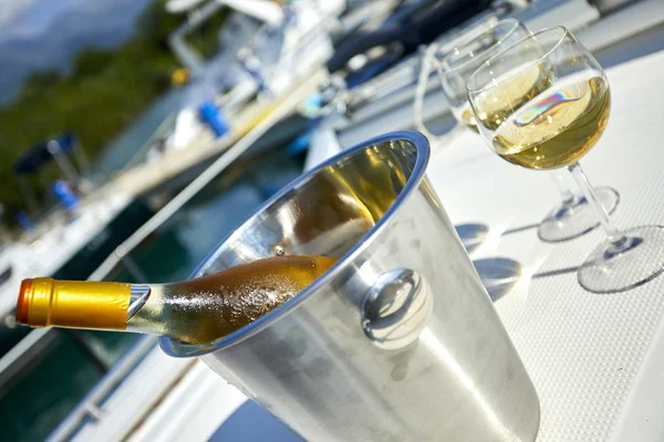 Pair of wineglasses with white wine and bucket with bottle on yacht