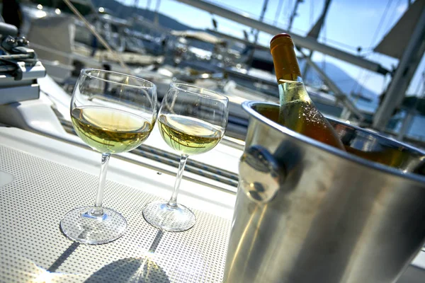 Pair of wineglasses with white wine and bucket with bottle on yacht