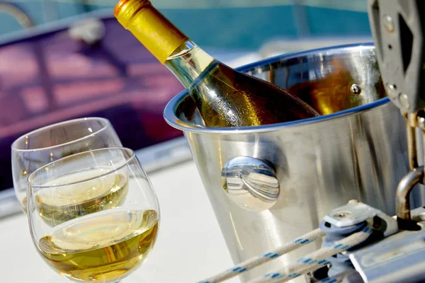 Pair of wineglasses with white wine and bucket with bottle on yacht