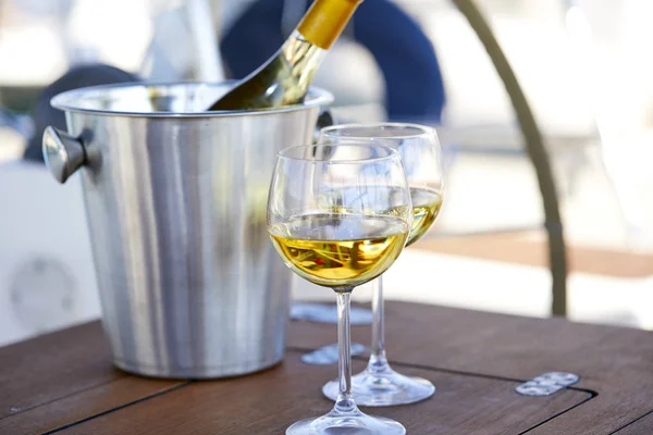 Pair of wineglasses with white wine and bucket with bottle on yacht