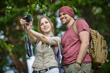 güneşli bir günde ormanda yürürken iki gezgin fotoğraf makinesinde selfie alıyor 