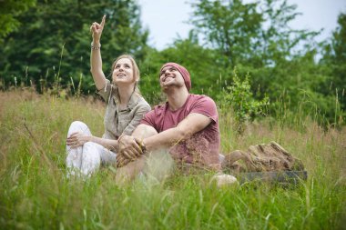 güneşli bir günde ormana yakın çayırda oturan iki gezgin 