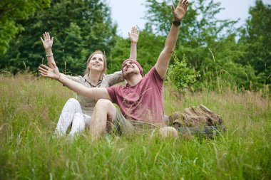 güneşli bir günde ormana yakın çayırda oturan iki gezgin 