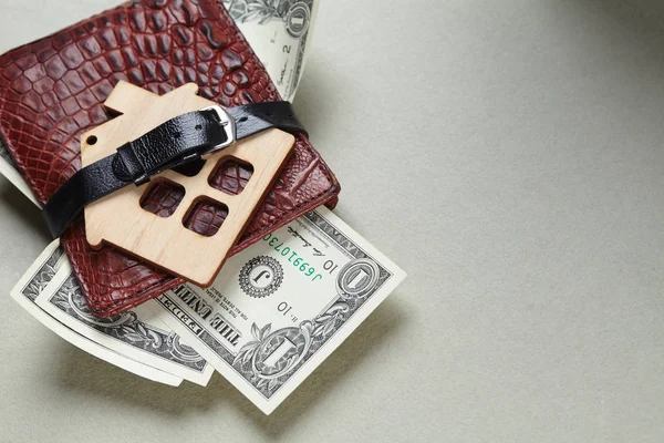 wallet with money and wooden house toy wrapped with belt, close-up