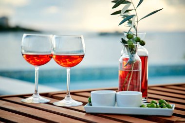 İskelede mavi suya karşı zeytinli iki bardak gül şarabı.