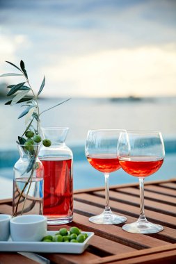 İskelede mavi suya karşı zeytinli iki bardak gül şarabı.