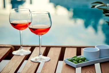 İskelede mavi suya karşı zeytinli iki bardak gül şarabı.