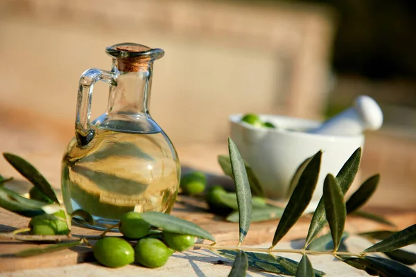 jug with olive oil and green olives on wooden background