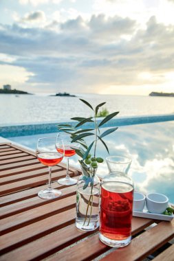 İskelede mavi suya karşı zeytinli iki bardak gül şarabı.