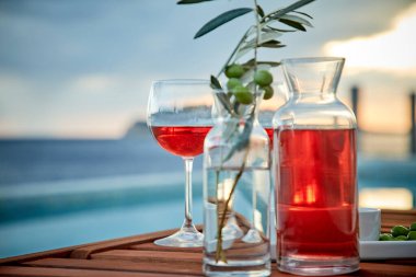 İskelede mavi suya karşı zeytinli iki bardak gül şarabı.