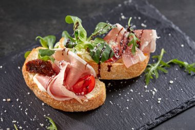 Koyu renkli taş tahtada etli ve sebzeli kanepeler, yakın görüş  