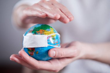 Koruyucu maskeli bir kadın dünyayı tutuyor.