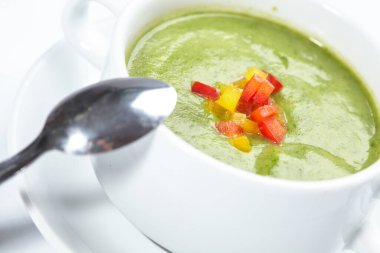 Beyaz kâsede kaşıklı yeşil kremalı çorba, yakın görüş. 