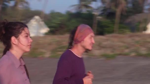 インドのゴア州の日没時にビーチでジョギングをする若いカップル — ストック動画