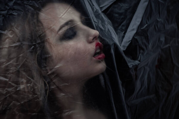 Молодая красотка грустная женщина заперта за пластиковым листом как защита от COVID-19. Красиво подходит для обложки книги 