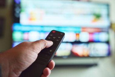 Bir insan büyük bir televizyonda uzaktan kumandayla kanal değiştiriyor, akşamları evde dinleniyor..