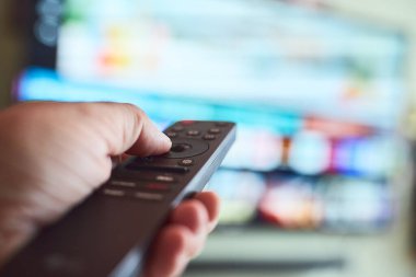 Bir el evdeki rahat bir akşamda televizyon kanallarını değiştirmek için uzaktan kumanda kullanıyor, rahatlatıcı bir atmosferle çevrili..