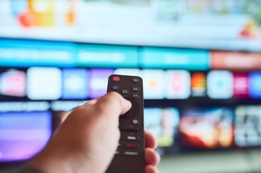 Uzaktan kumandayla televizyonu kontrol eden bir kişi, evde rahat bir akşam boyunca çeşitli eğlence seçeneklerini değerlendirir..