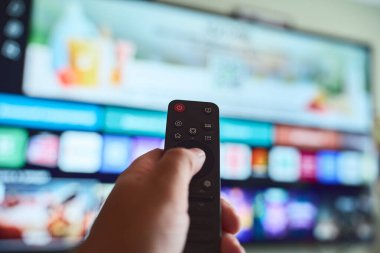 Bir el, oturma odasındaki akıllı bir televizyonda çeşitli menü seçeneklerini gözden geçirirken uzaktan kumandayı tutuyor..