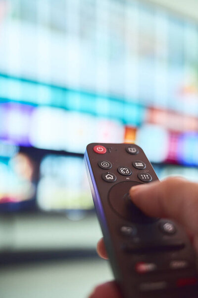 A hand holds a remote control while tuned into a colorful display of content on a large screen in a modern living room.