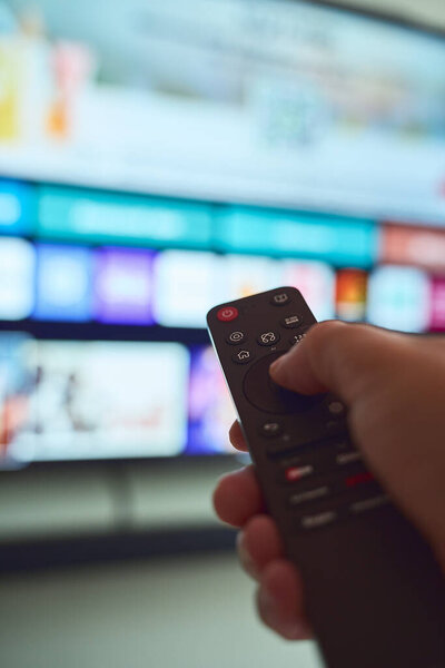 A person controls a smart TV with a remote, selecting shows amid vibrant content options displayed on the screen.